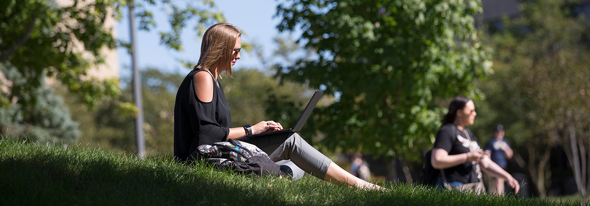 student sitting on grass working on laptop