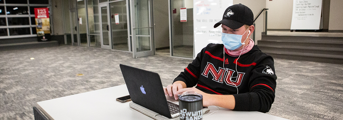 student wearing mask working on laptop